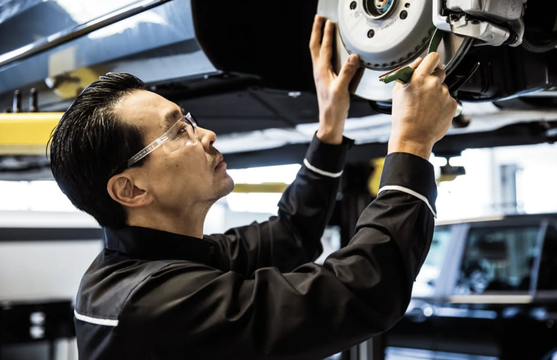 Mercedes-Benz technician measuring brake pad wear on a lifted vehicle during service in Orlando, FL
