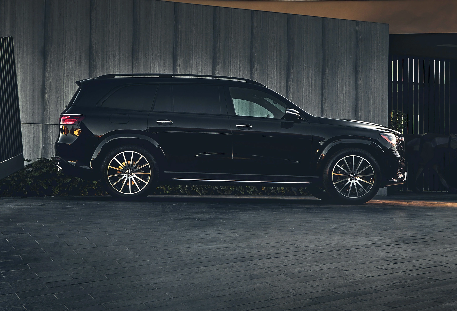 A black Mercedes-Benz GLS parked outside a modern home in the evening, side view