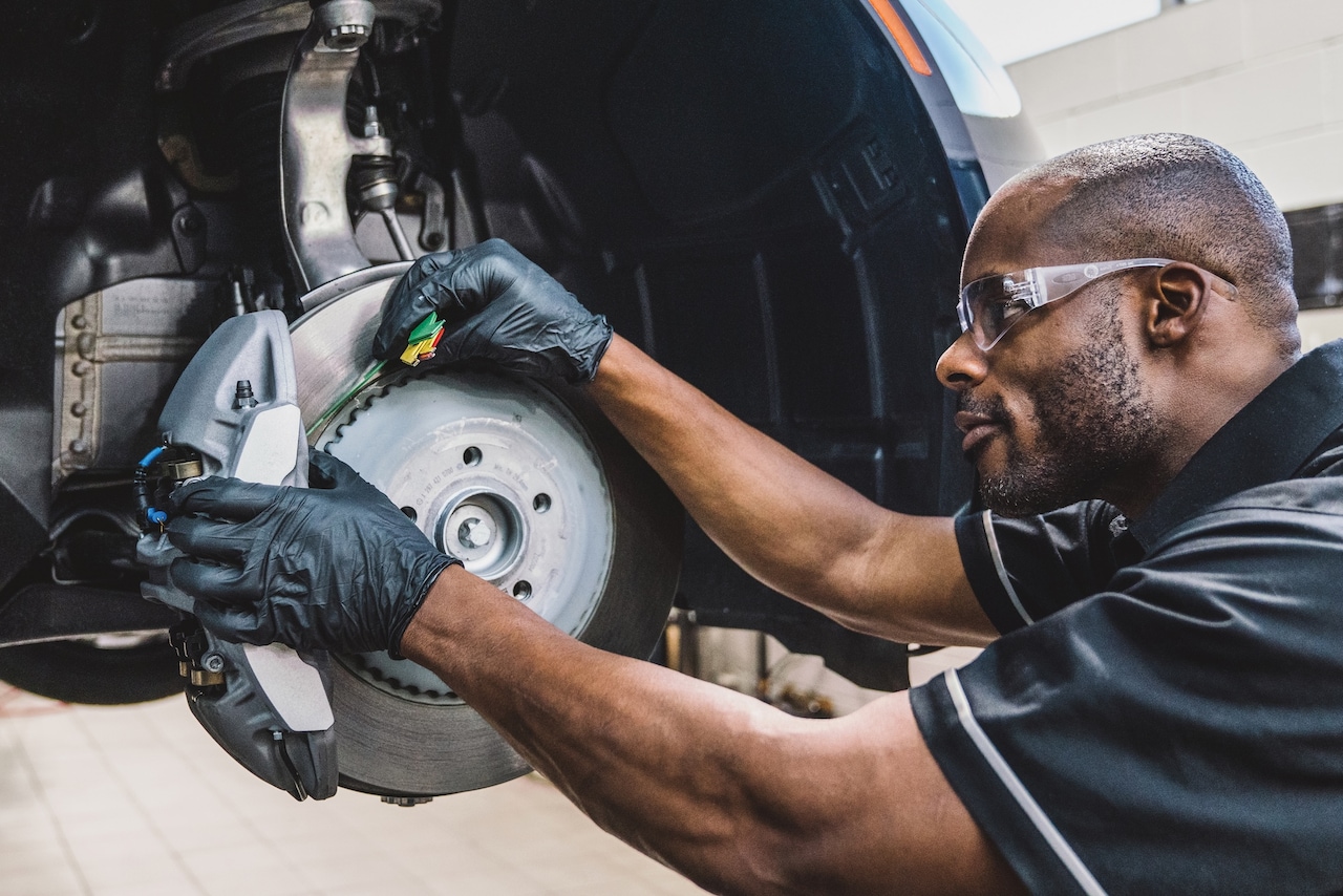 A Mercedes-Benz technician fitting a brake pad to the disc of a raised car