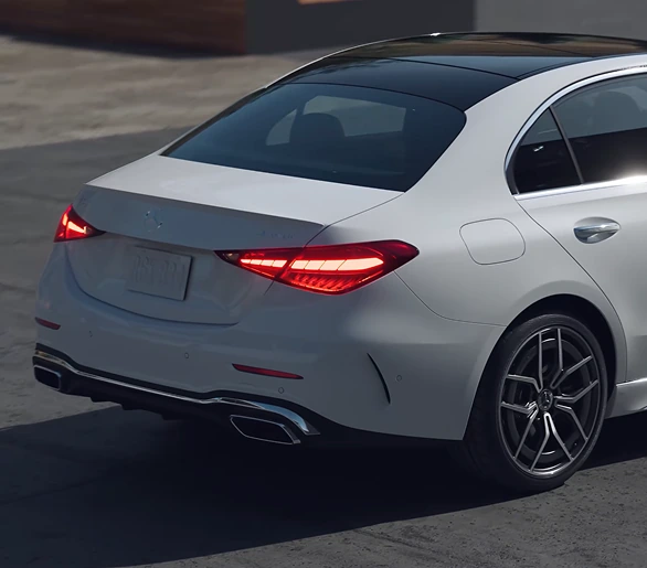 Rear three-quarter view of a white C-Class Sedan with its LED taillamps lit