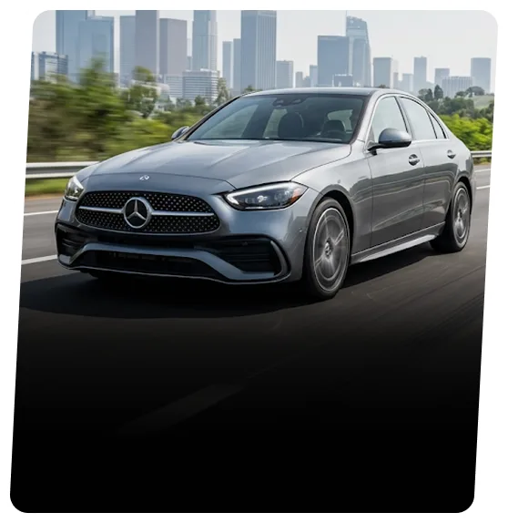 Silver Mercedes-Benz sedan on a highway with a city skyline behind