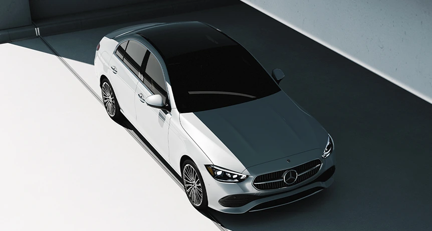 Overhead view of a white C-Class Sedan with a black panoramic roof parked in angled light and shadow