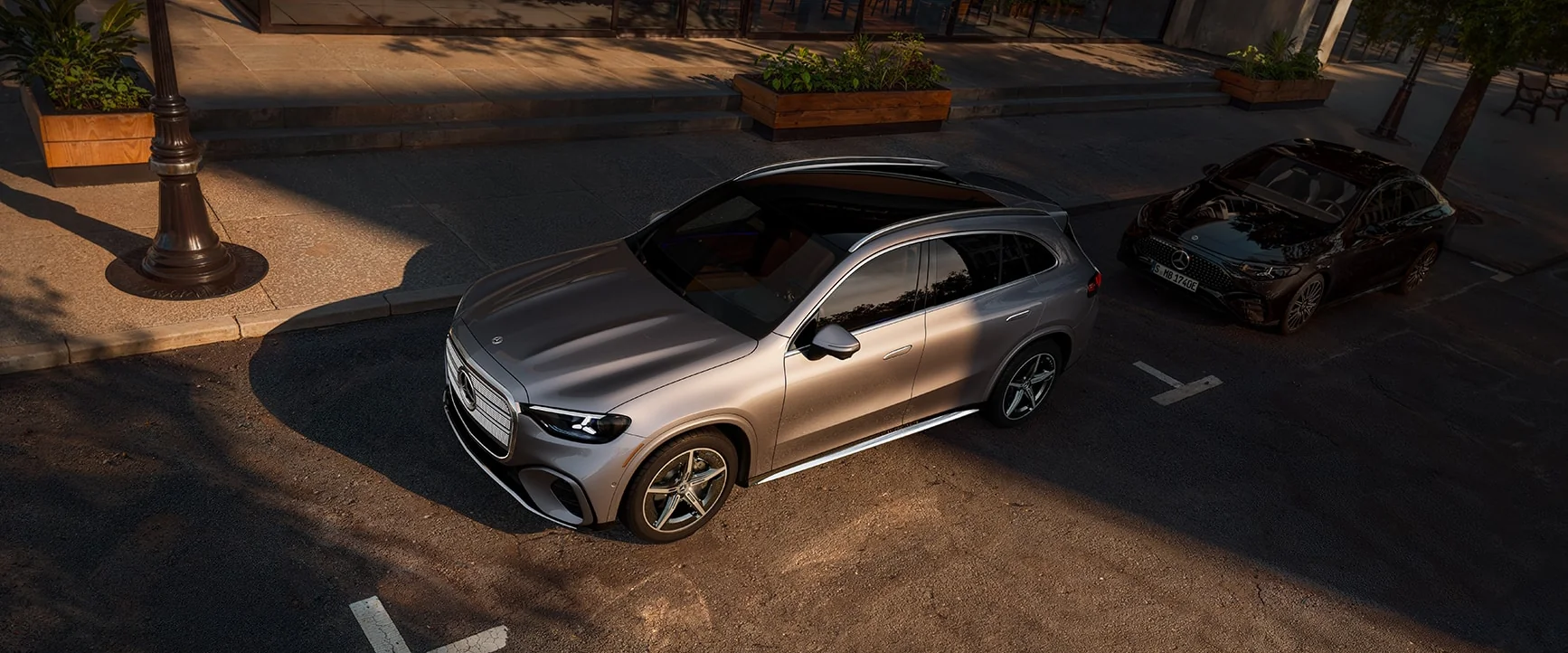 A silver Mercedes-Benz GLC parked in a street bay outside a cafe, seen from above