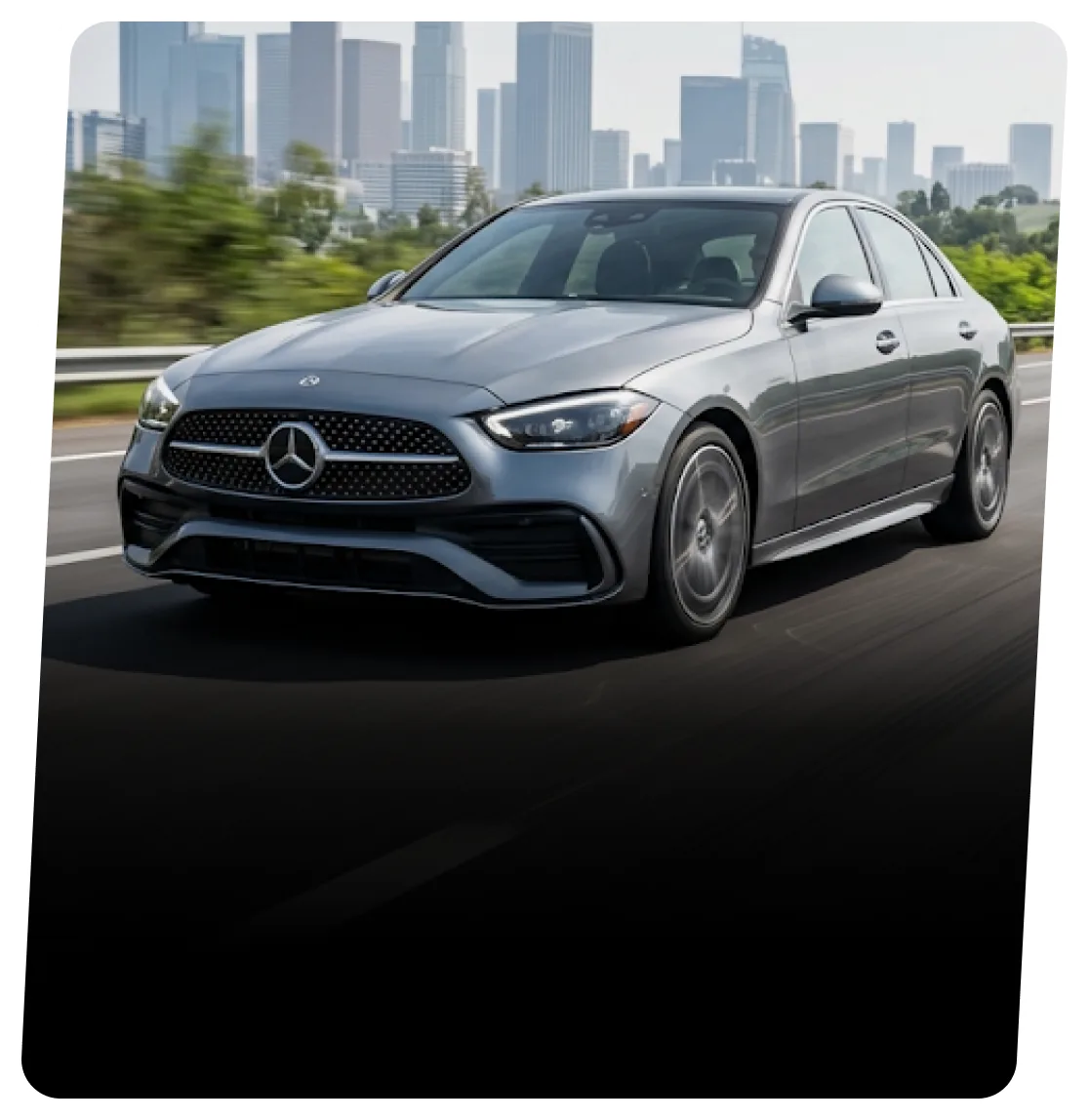 Silver Mercedes-Benz sedan on a highway with a city skyline behind