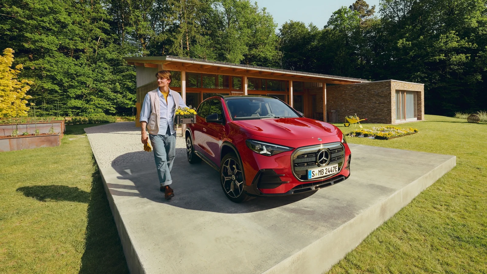 A red Mercedes-Benz GLA parked outside a modern garden pavilion, a person walking toward the camera carrying flowers