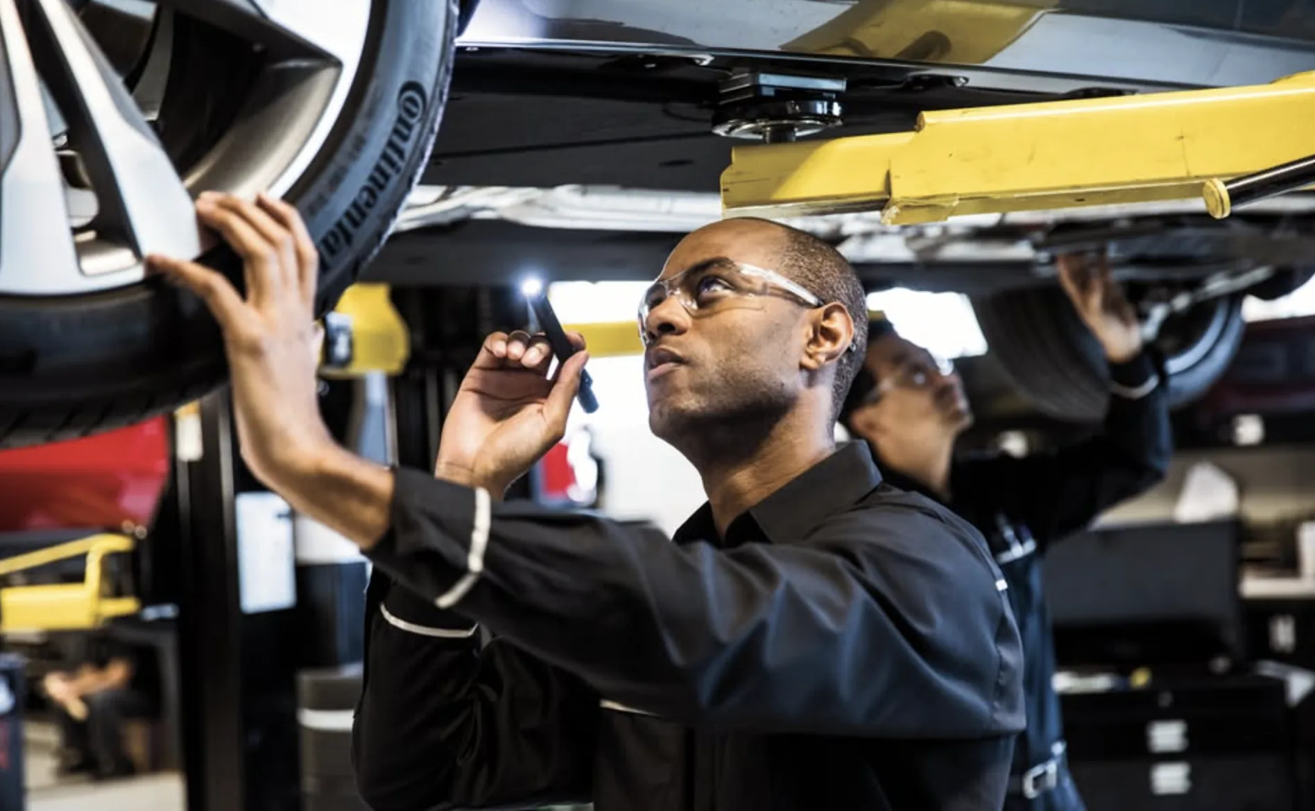 Mercedes-Benz technicians inspecting a tire and underbody with a flashlight on a lifted vehicle in Orlando, FL