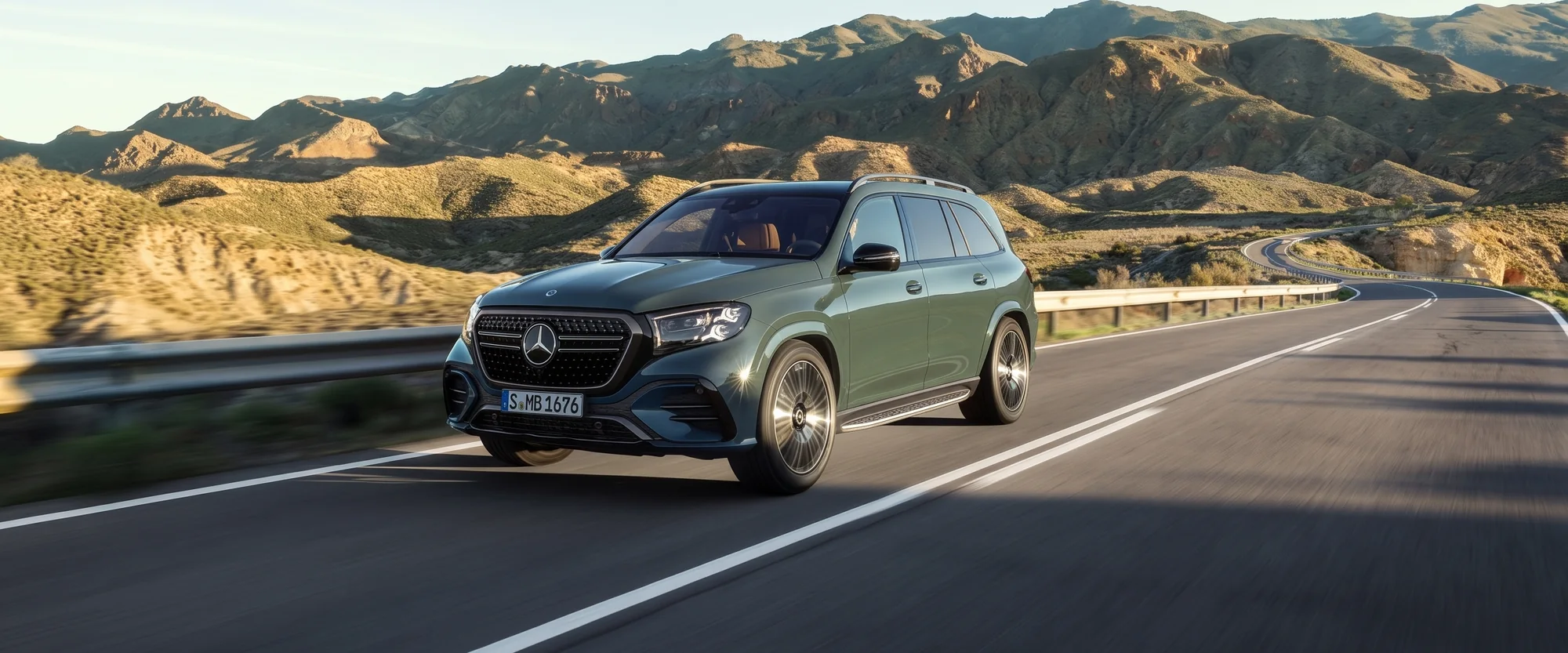 A dark green Mercedes-Benz GLS driving a mountain highway at golden hour, front three-quarter view