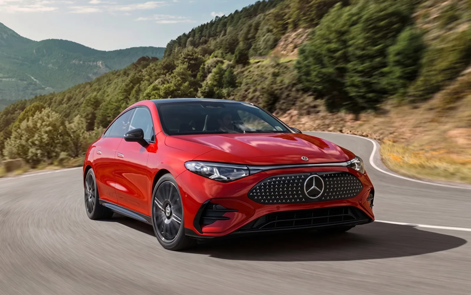 A red Mercedes-Benz EQE sedan driving a winding mountain road, front three-quarter view