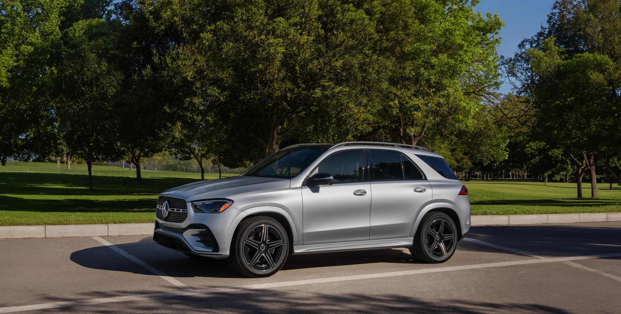 A silver Mercedes-Benz GLE SUV parked in a lot, front three-quarter view, with green trees behind