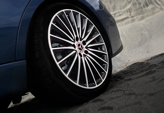 Close-up of a multi-spoke two-tone alloy wheel on a blue C-Class Sedan on a sandy surface