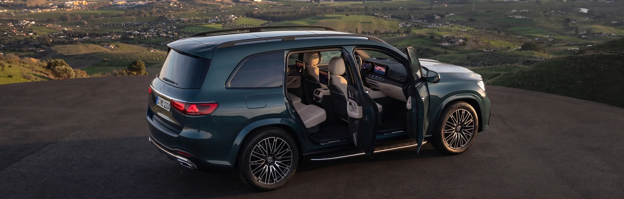 A green Mercedes-Benz GLS parked on a hilltop overlook with both side doors open, the seats inside in view
