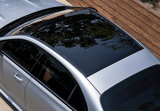 High angle of a silver C-Class Sedan roof showing the glass Panorama sunroof reflecting trees