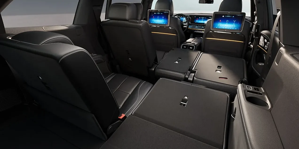 The second row of a Mercedes-Benz GLS in black leather seen from the cargo area, rear entertainment screens on the front seat backs and the third row folded flat