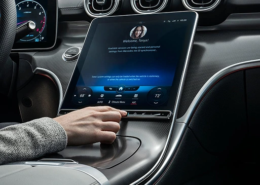 Driver resting a finger on the console fingerprint scanner below the C-Class touchscreen showing a welcome profile