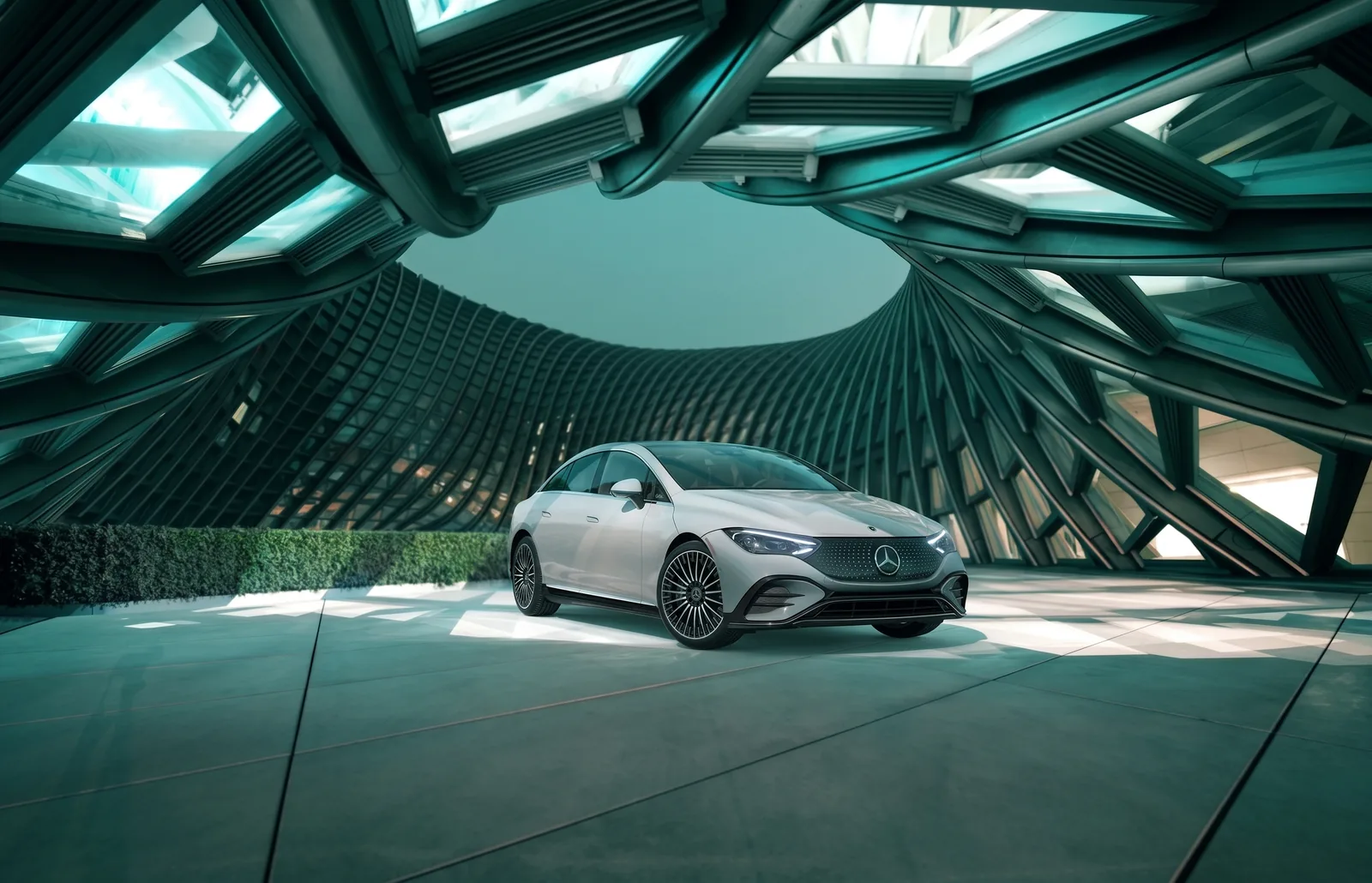 A silver Mercedes-Benz EQE sedan parked under a curved green lattice canopy, front three-quarter view