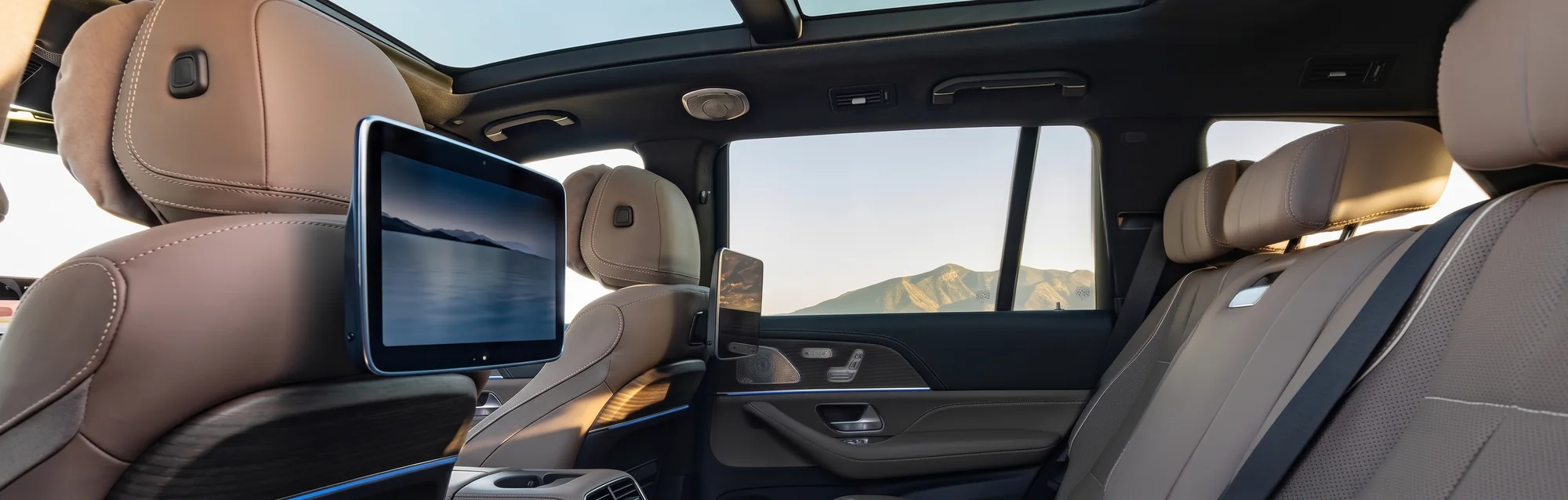 The middle-row captain's chairs of a Mercedes-Benz GLS in beige leather, a rear entertainment screen on the seat back and mountains through the side window
