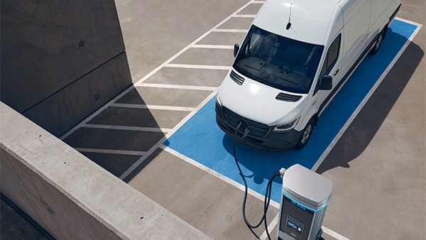 Exterior shot of a Mercedes-Benz eSprinter Van parked at a charging station on the top floor of a parking garage.