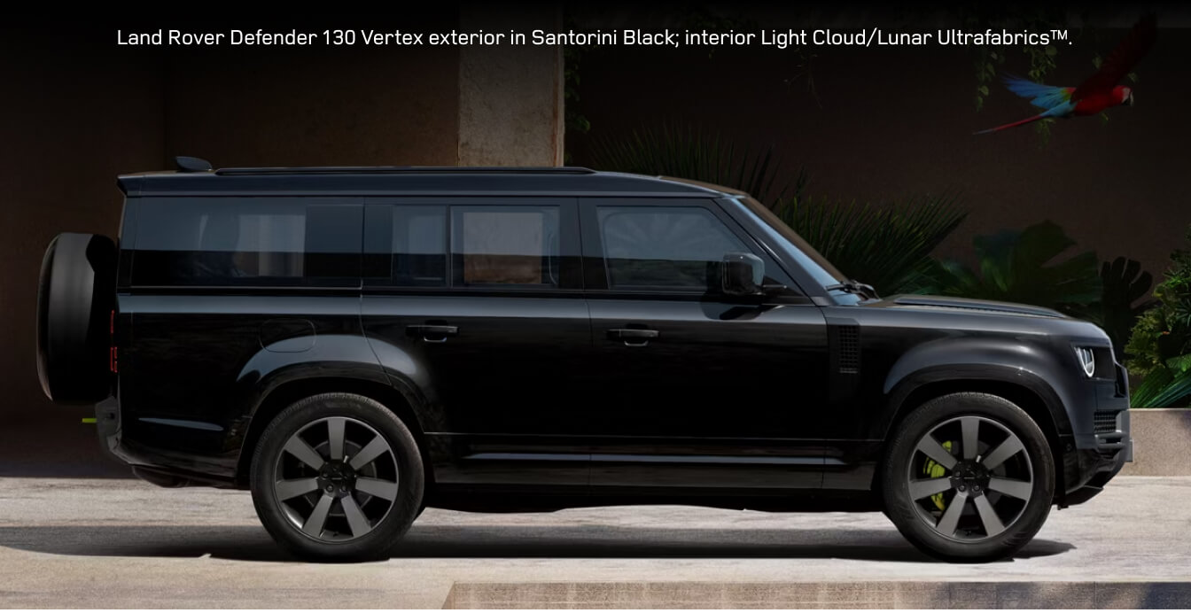 Profile view of a extended 2026 Land Rover Defender 130 Vertex in Santorini Black parked outside a modern building.