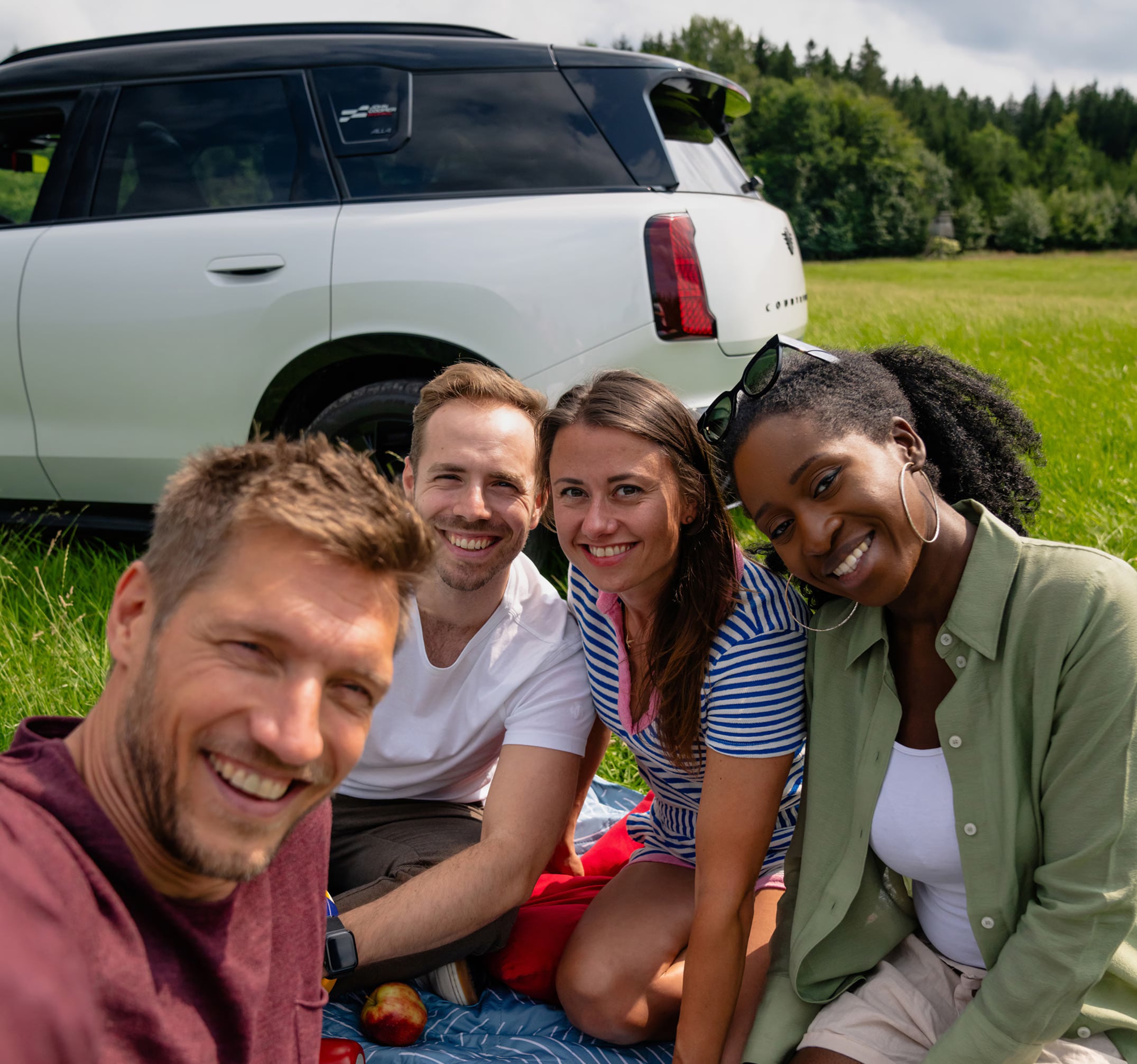 Four college students in front of the rear of a white MINI parked on a grass field.