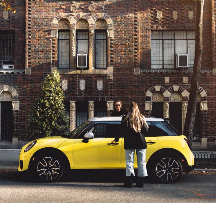 Two college students about to get into a yellow MINI 4 Door parked in front of a brick building.