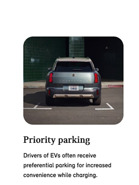 Three-quarters front view of a MINI Electric vehicle parked on a cobblestone surface in a parking space in front of a retail storefront in an urban setting.
