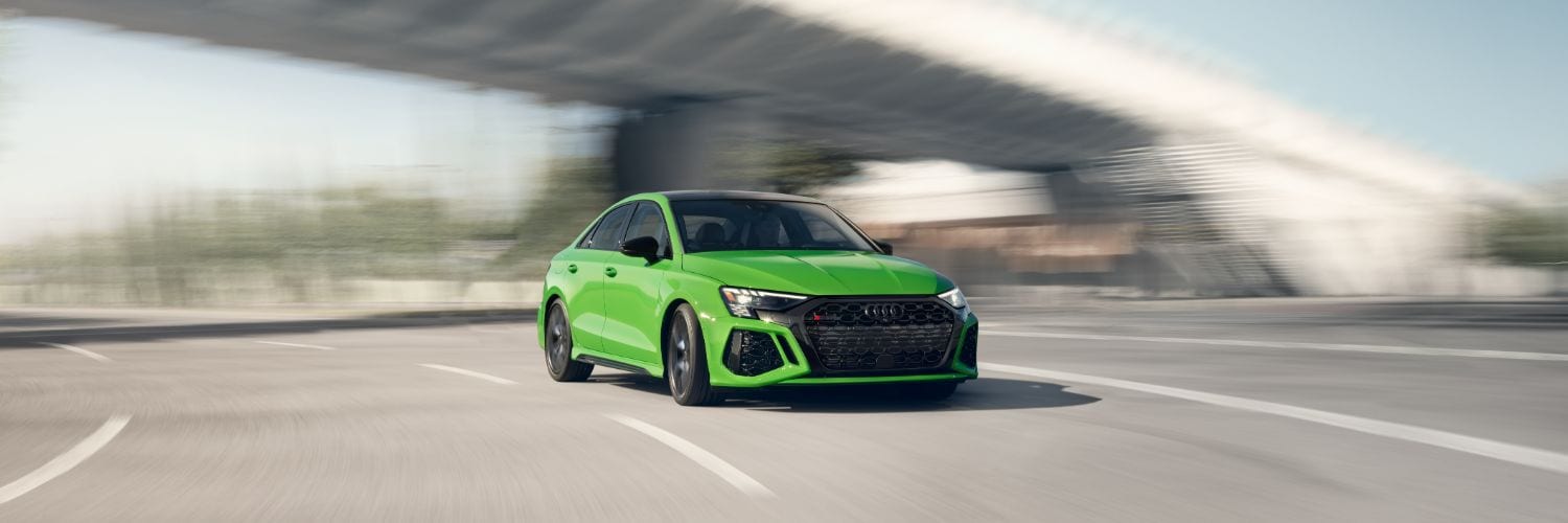 Green Audi RS 3 driving fast on a curved highway