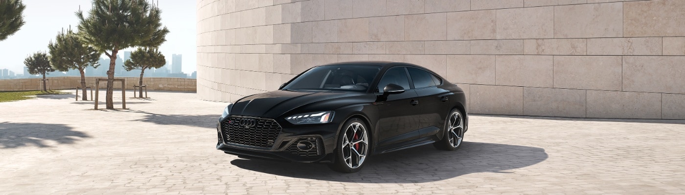 Black Audi RS 5 parked on a modern road near trees