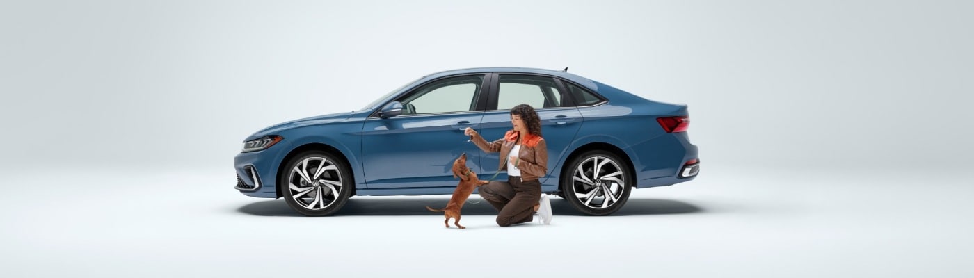 Woman and small dog next to a blue VW Jetta