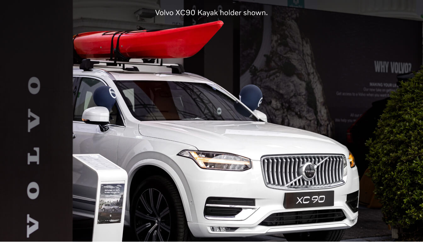 Three-quarter front view of a Crystal White Volvo XC90 Ultra with a red kayak on its roof rack.