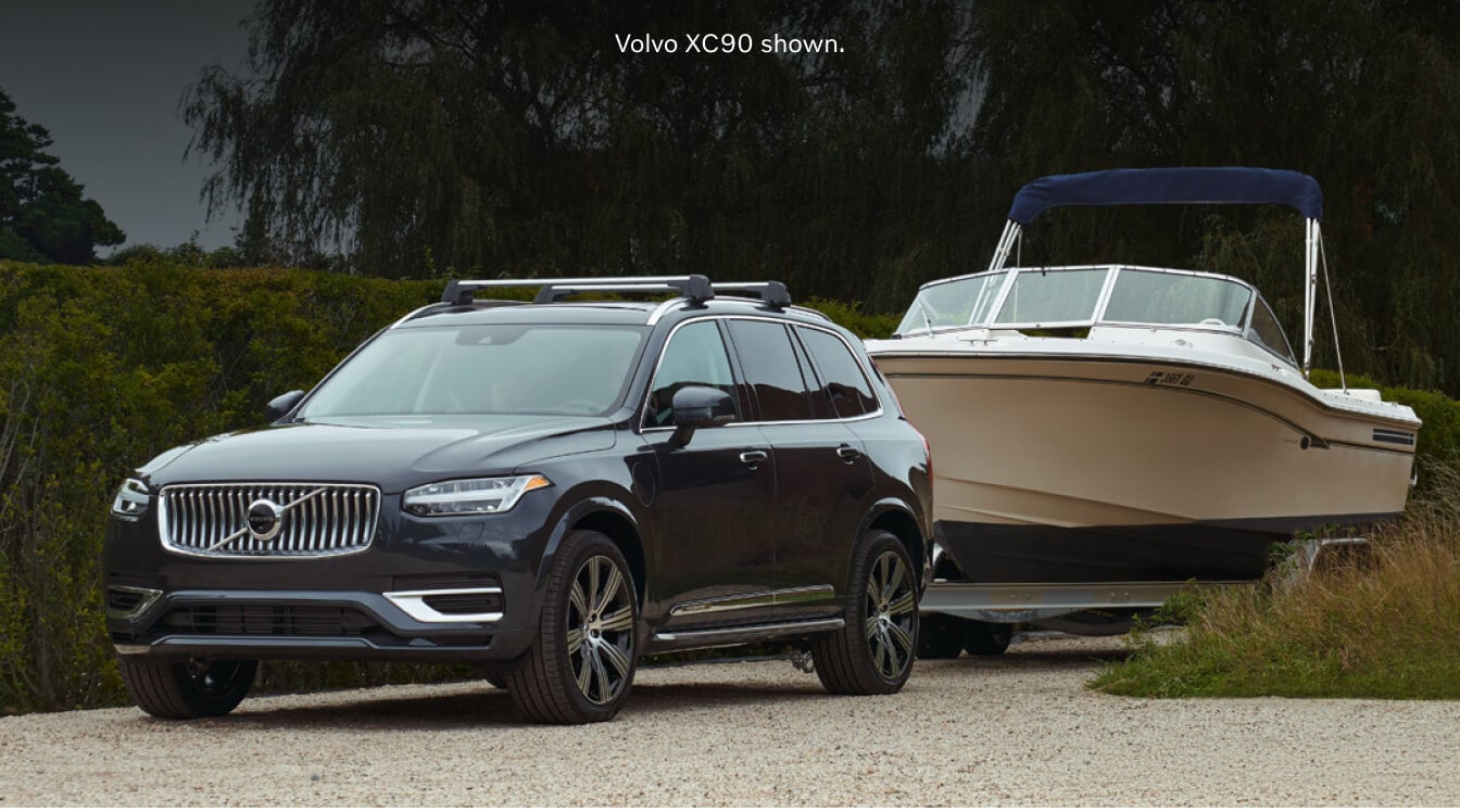 Front-quarter view of a Platinum Grey Volvo XC90 Ultra towing a motorboat down a gravel trail.