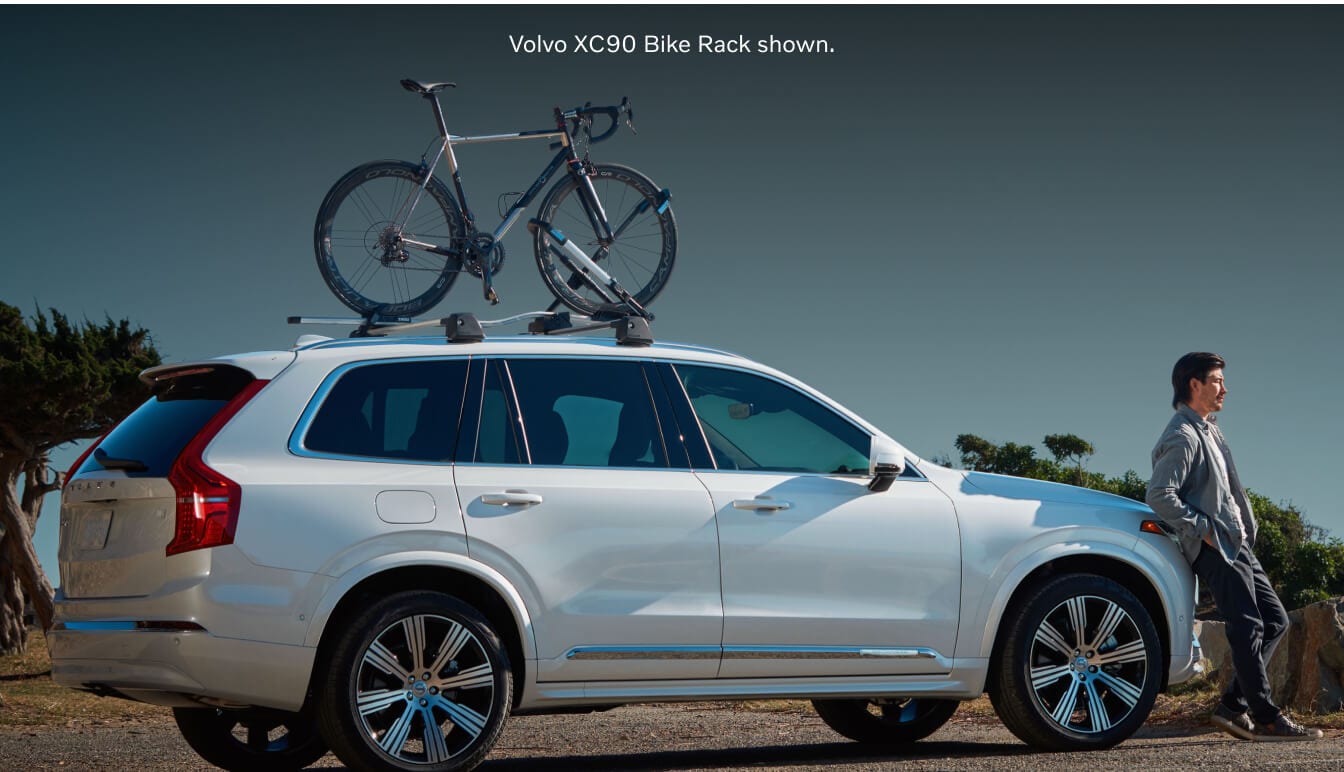 Side-profile view of a Crystal White Metallic Volvo XC90 Ultra carrying a bicycle on its roof rack.