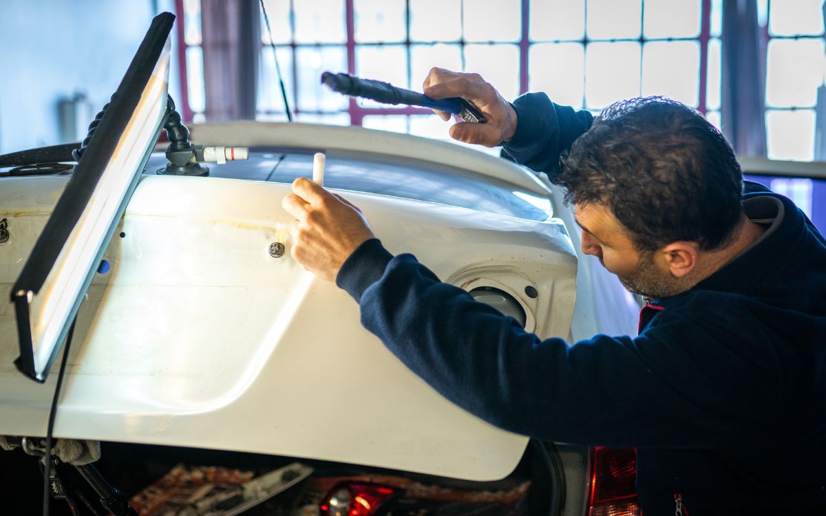 man performing paintless dent repair on trunk of sedan