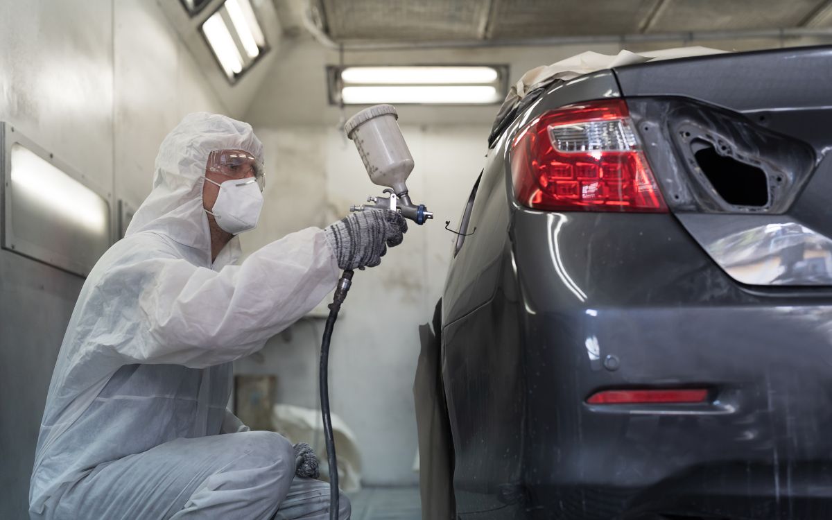 man using a spray gun to paint rear bumper of car