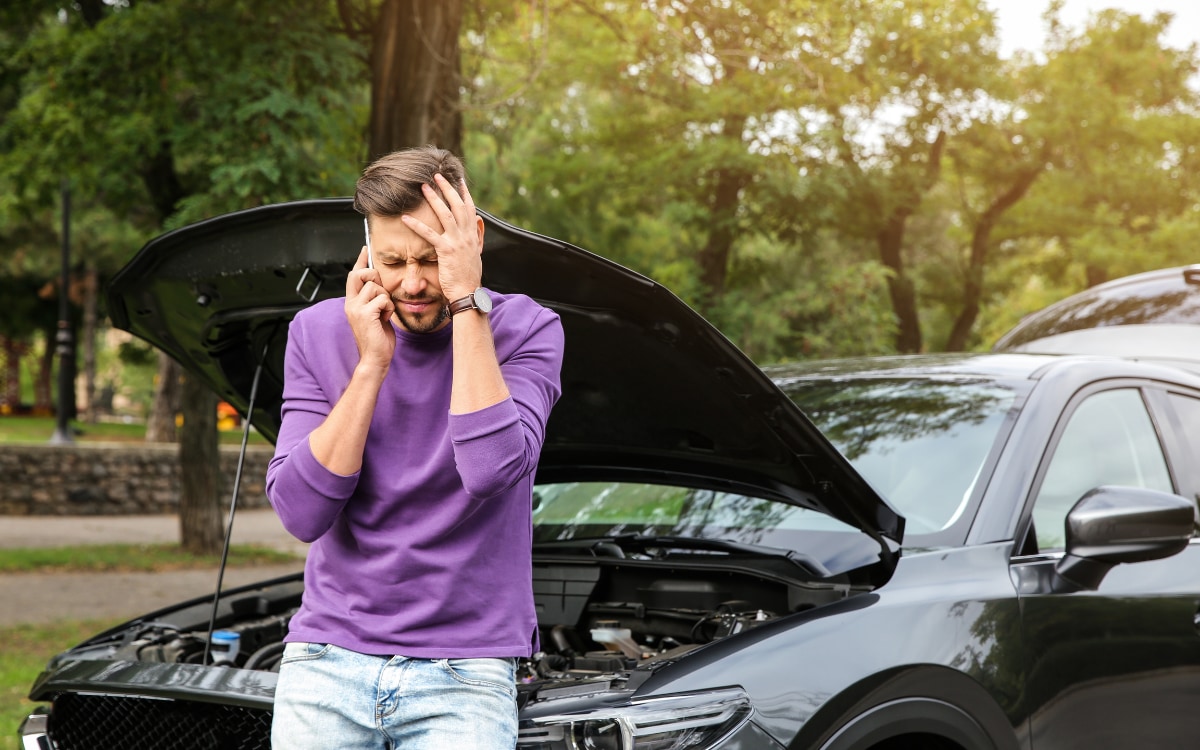 Man speaking with insurance next to broken car