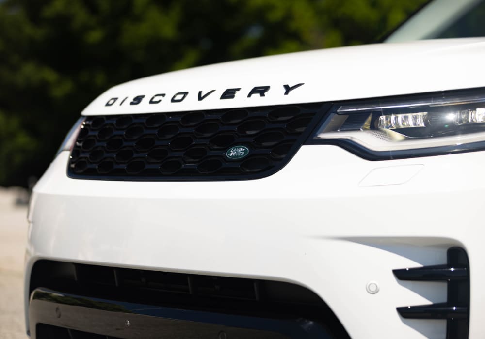 2025-land-rover-discovery.png Close up shot of the front grille of the Land Rover Discovery SUV. The Land Rover logo is visible on the right side of the front grille
