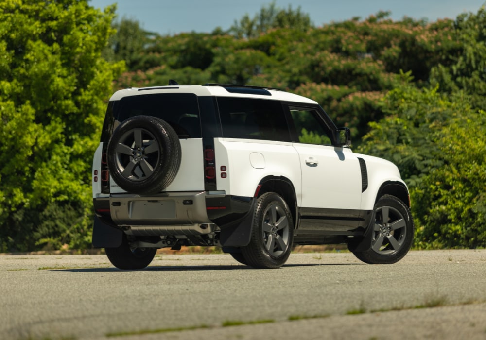 2025-defender-90-greensboro-nc.png Rear exterior view of a 2025 Land Rover Defender 90 for sale in Greensboro. The SUV is white and parked on a paved lot