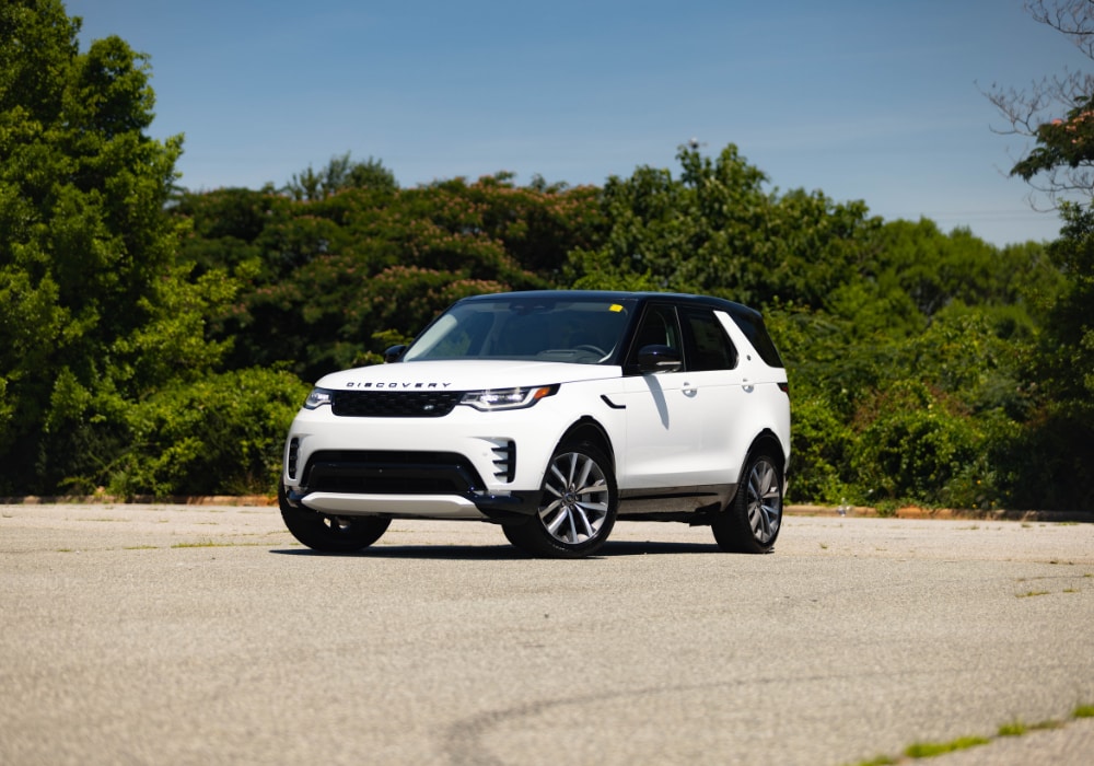 land-rover-discovery-suv-for-sale.png 2025 Land Rover Discovery for sale. The SUV is white and parked on a paved lot in front of trees