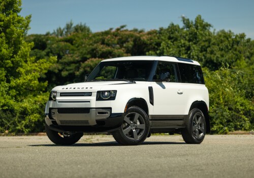 defender-90-for-sale.png White Land Rover Defender 90 parked on a paved surface with trees in the background