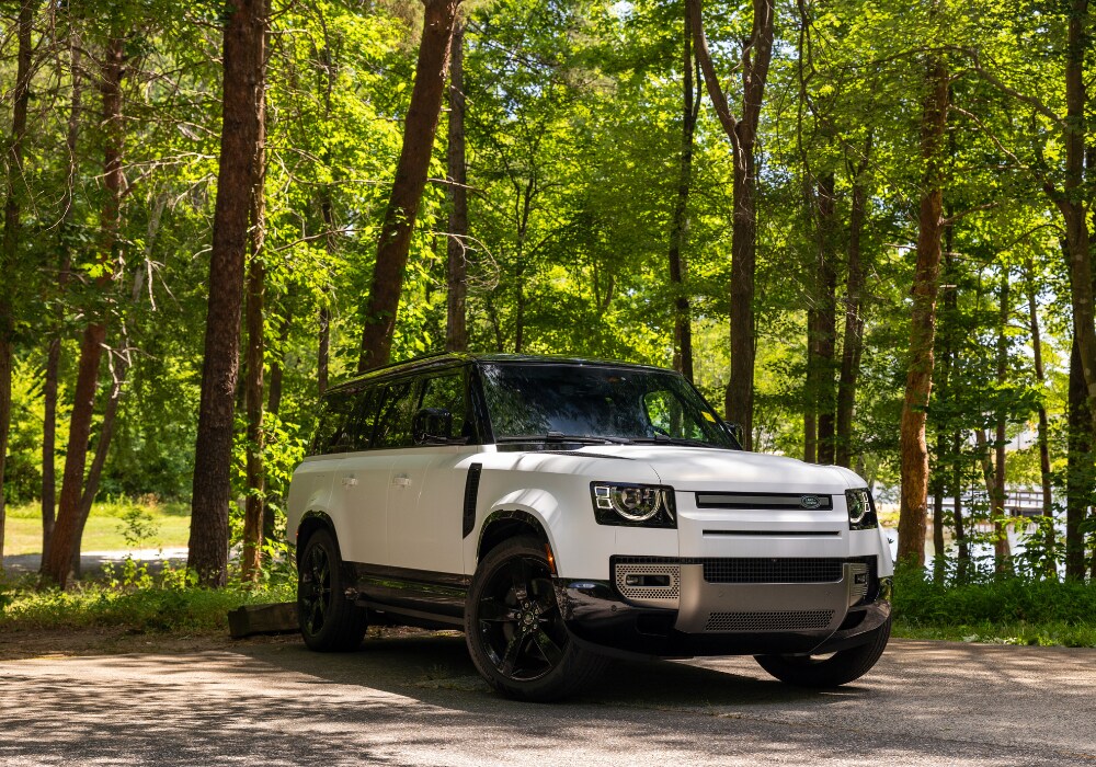 2024 Land Rover Defender parked in a wooded area. The SUV is white