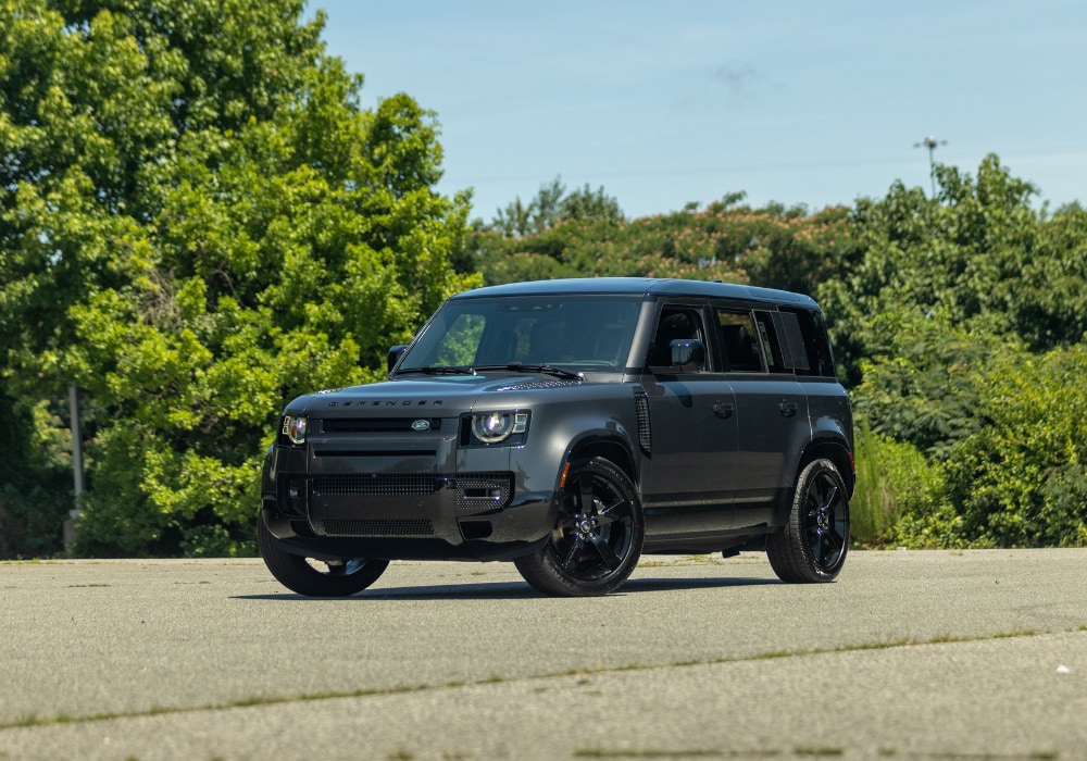 2025-defender-110-greensboro-nc.png Land Rover Defender 110 parked in a paved lot with a tree line in the background