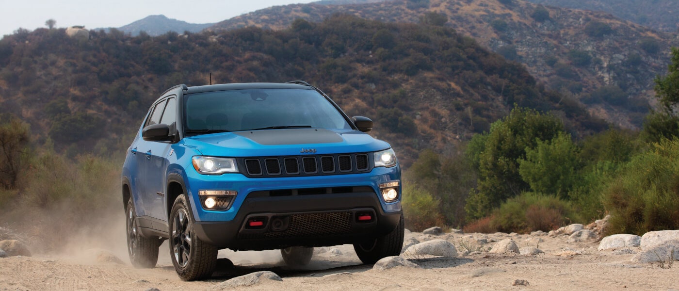 2020 Jeep compass in blue driving on dirt road with mountians behind it