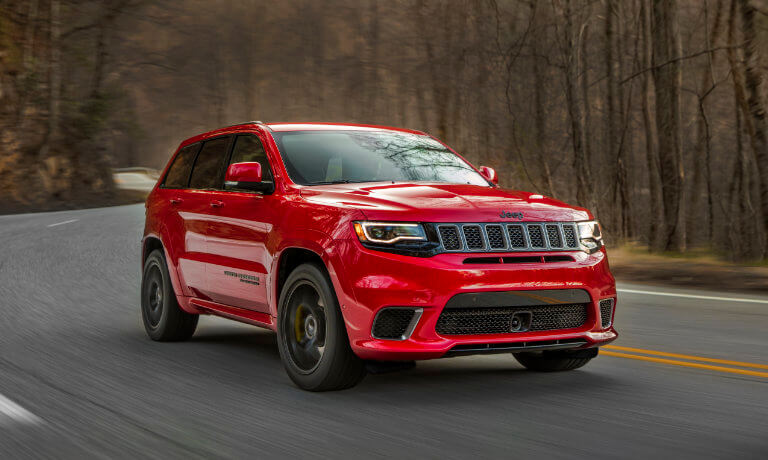 2020 Jeep Grand Cherokee in red driving on highway throughout the forest