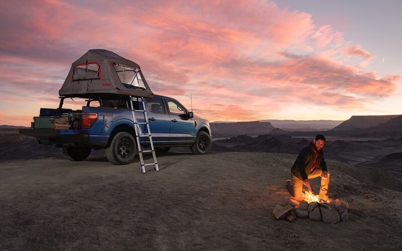 Ford F-150 parked in desert with tent attached to roof while man stokes fire nearby from Used Car Dealer near Coon Rapids MN