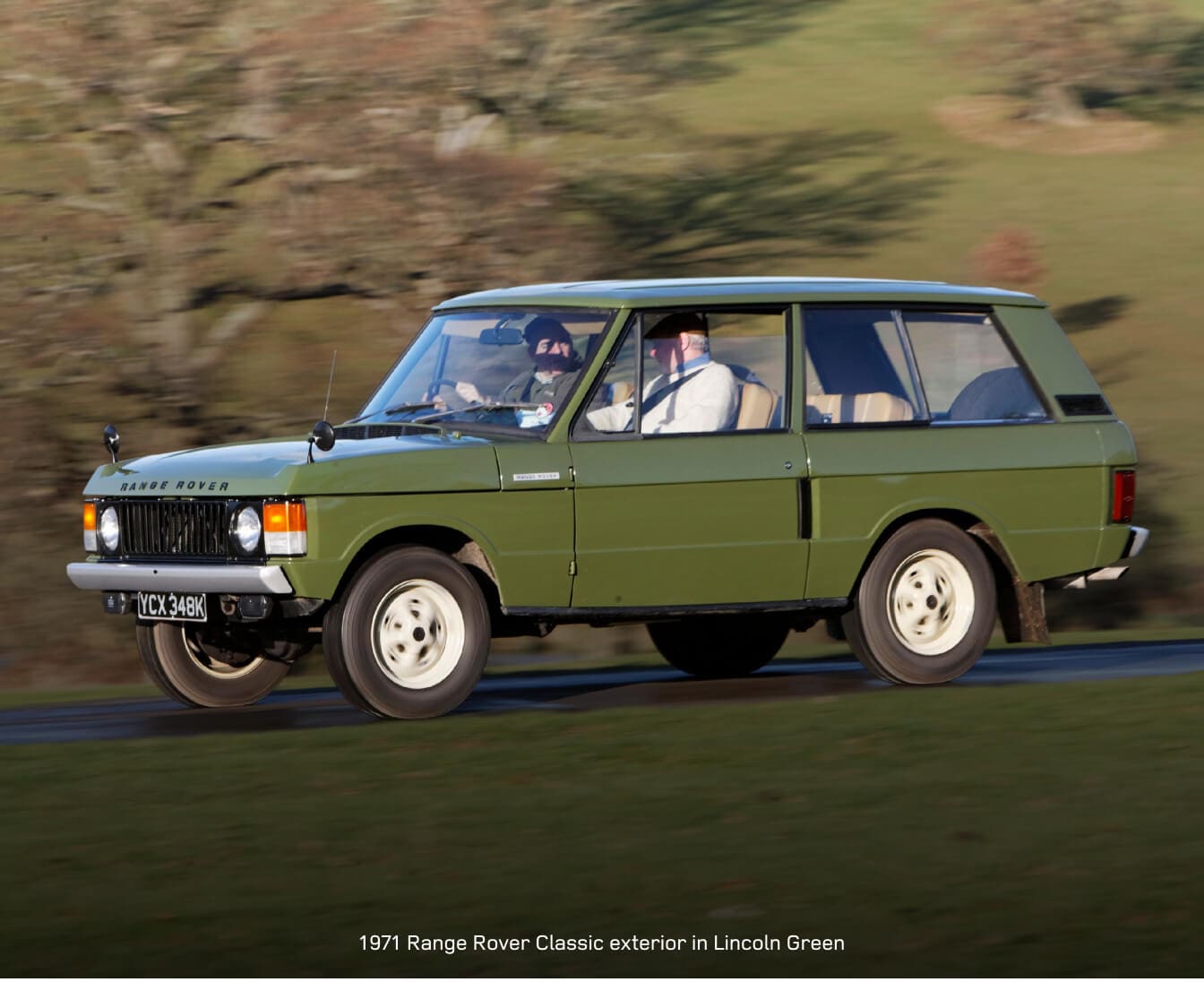 1971 Range Rover Classic drives along a country road in a green hillside setting.