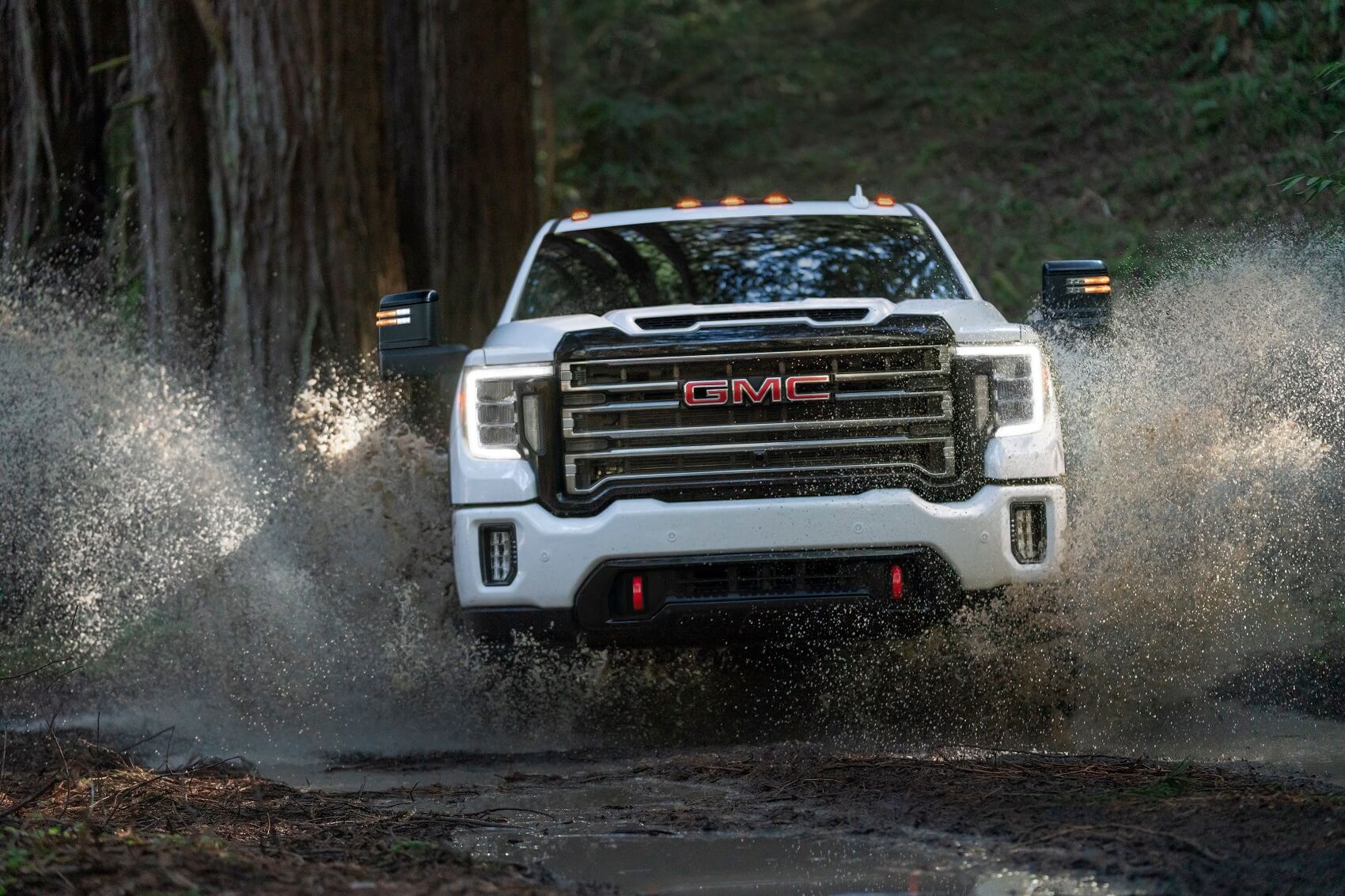 Front view of Used GMC Sierra 2500 driving through water in the woods with water splashing up around vehicle