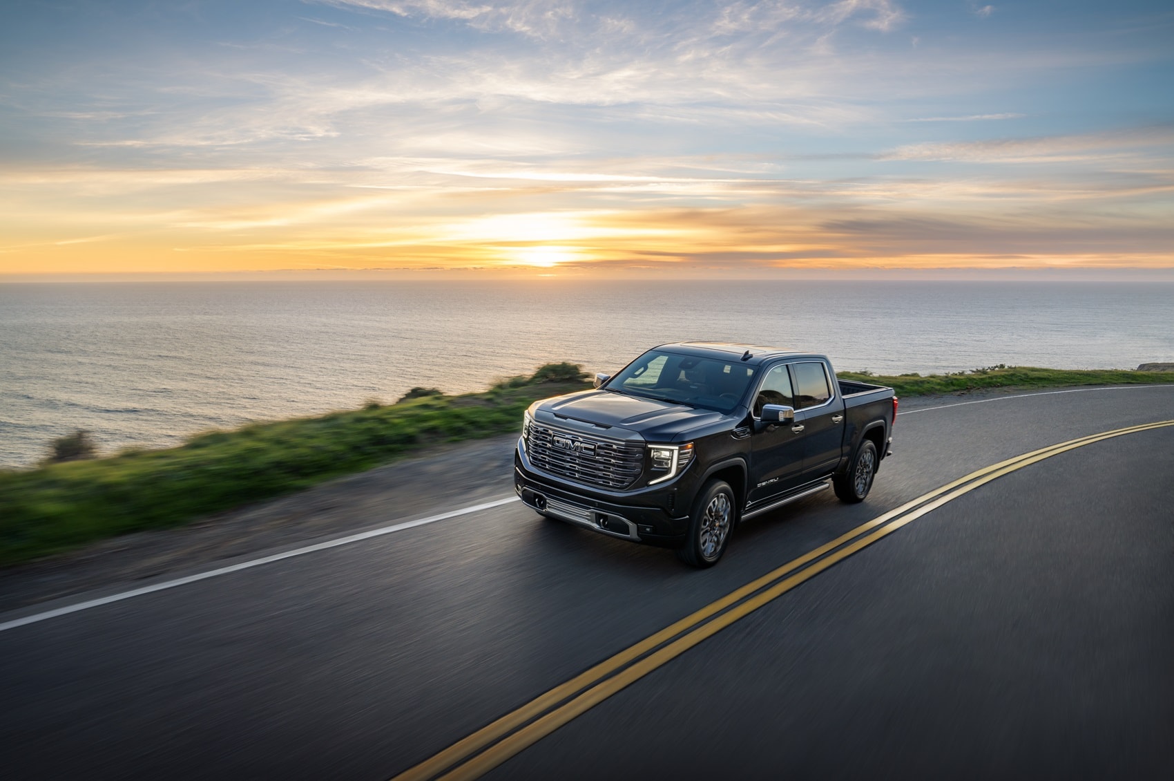 Used GMC Silverado truck driving along coastal road with sunset background