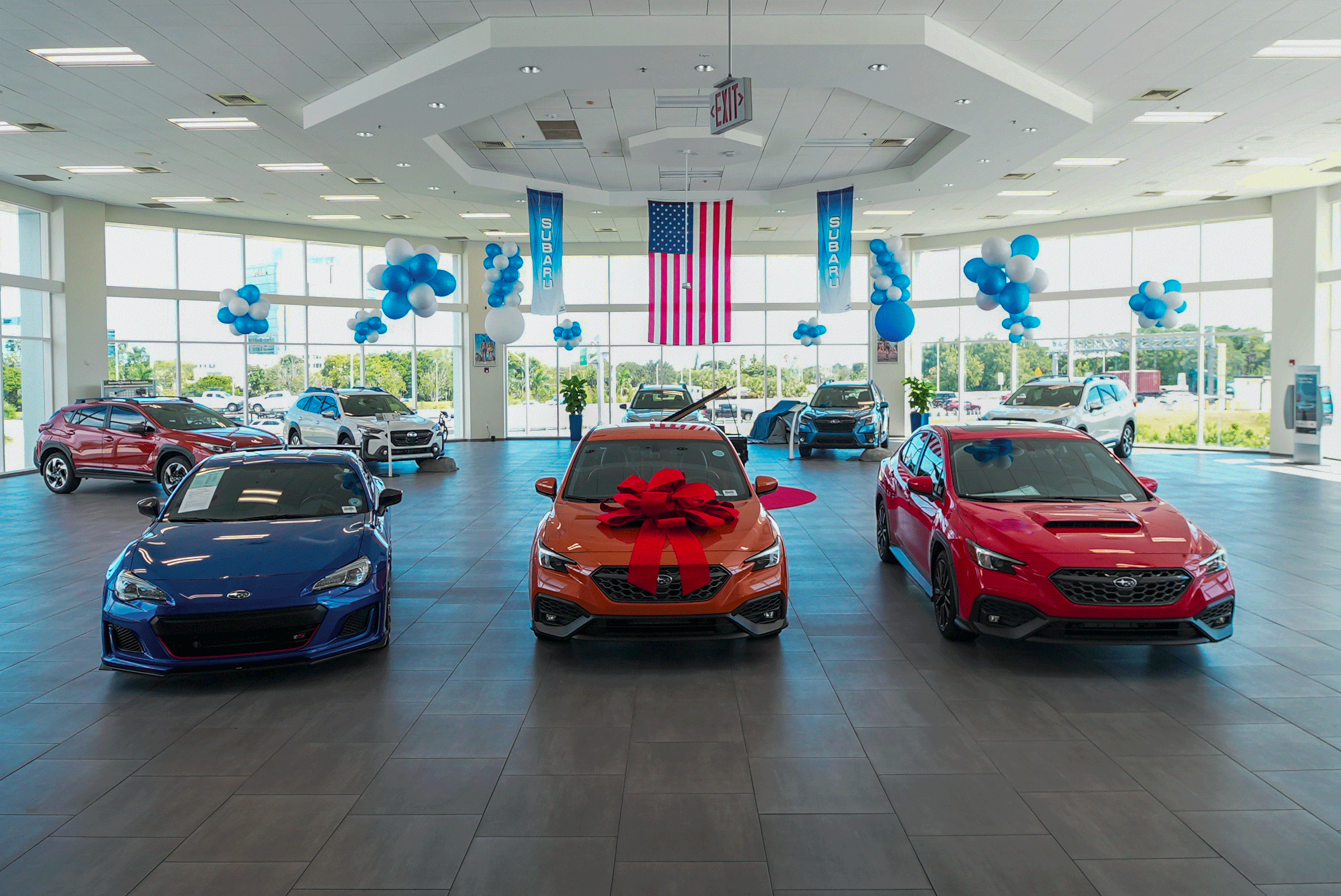 Blue, orange, and red Subaru cars displayed inside North Fort Lauderdale Subaru, with a red bow on the orange sedan.
