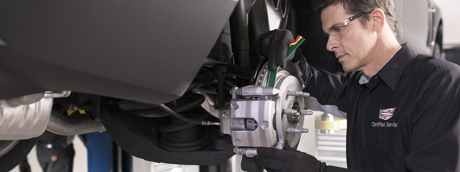 Cadillac Certified Service technician inspecting a front brake rotor and caliper at Ocean Cadillac in Miami