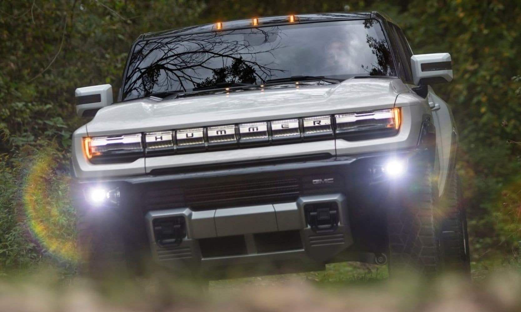 Image of a 2022 GMC Hummer EV truck driving into the lens of the camera with glaring LED fog lights