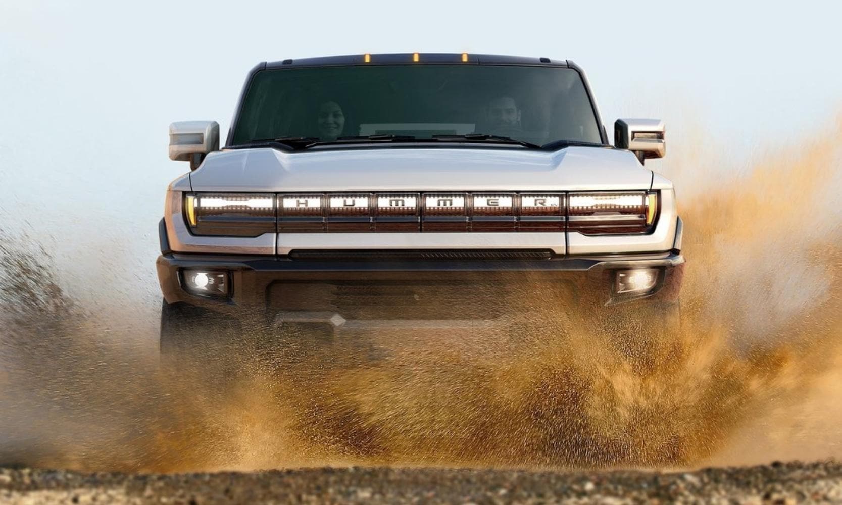 Image of the front of a 2024 GMC Hummer SUV plowing through heavy sand driving into the camera lens